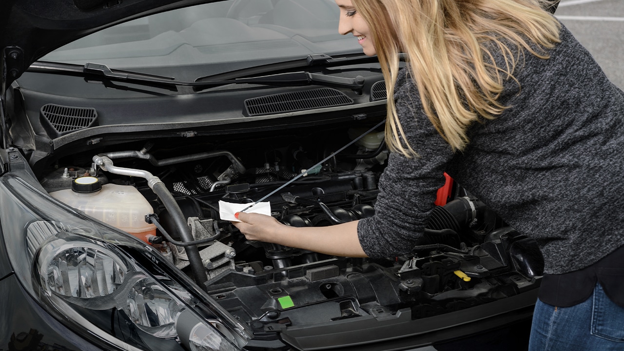 Autofahrerin prüft den Ölstand mit Peilstab zur regelmäßigen Wartung.