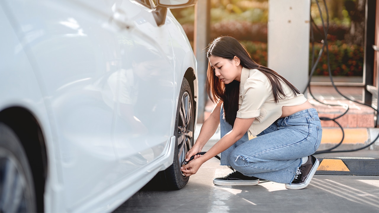 Autofahrerin überprüft den Reifendruck für Sicherheit und geringeren Verbrauch.