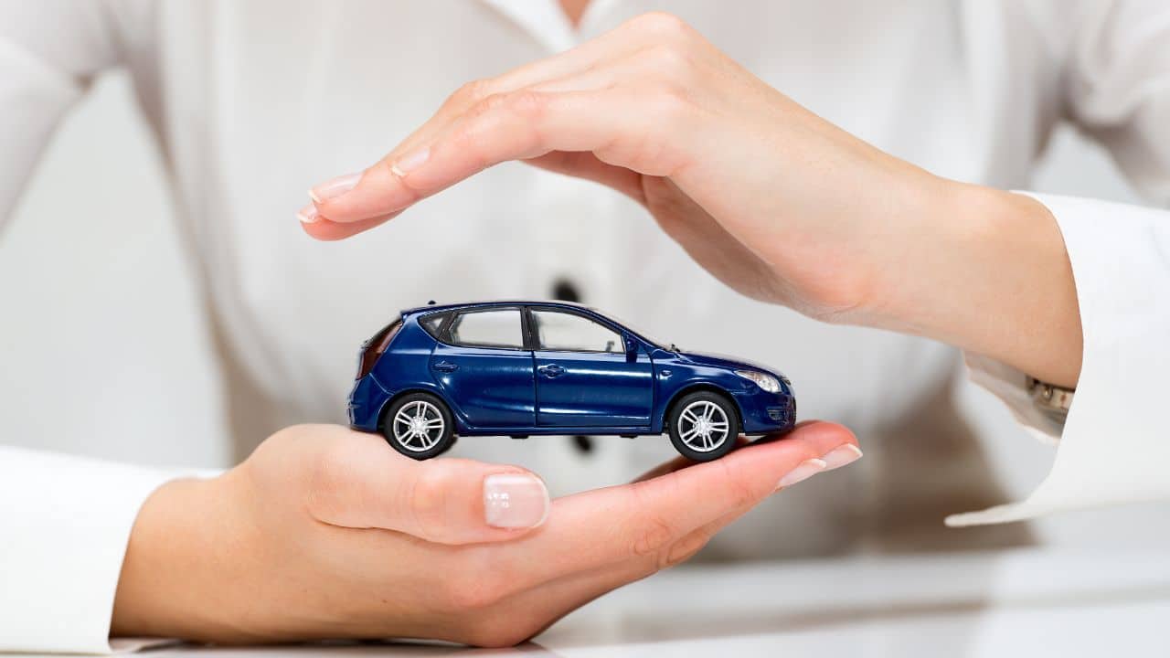 Schützende Hände um ein blaues Modellauto als Sinnbild für mehr Sicherheit im Straßenverkehr durch verpflichtende Assistenzsysteme im Auto seit 2025.